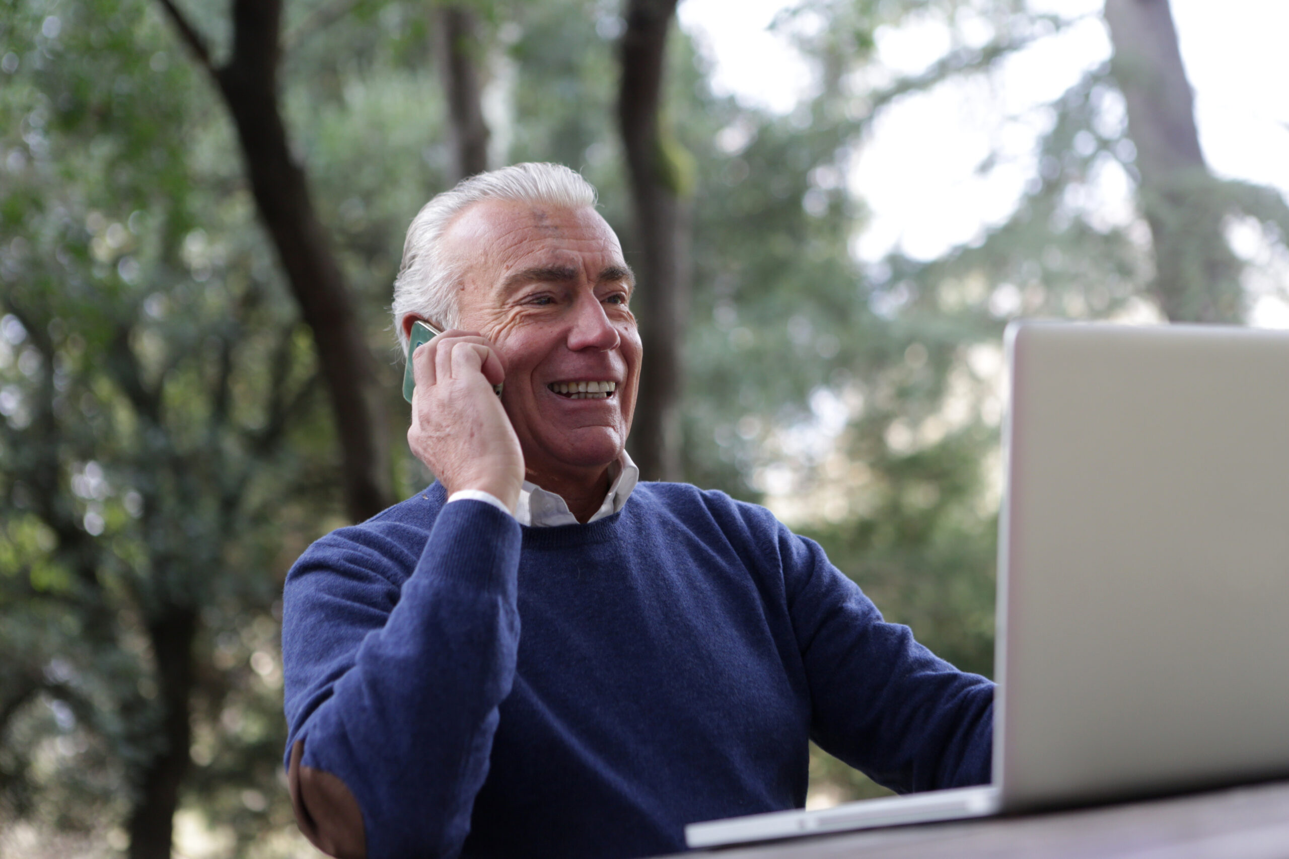 older financial professional talking on cell phone while reviewing client information on laptop