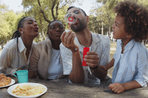 static image of family sitting at picnic table with child blowing bubbles