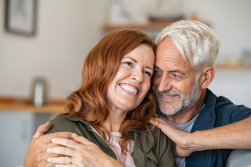 Cheerful mature couple embracing while sitting on couch.
