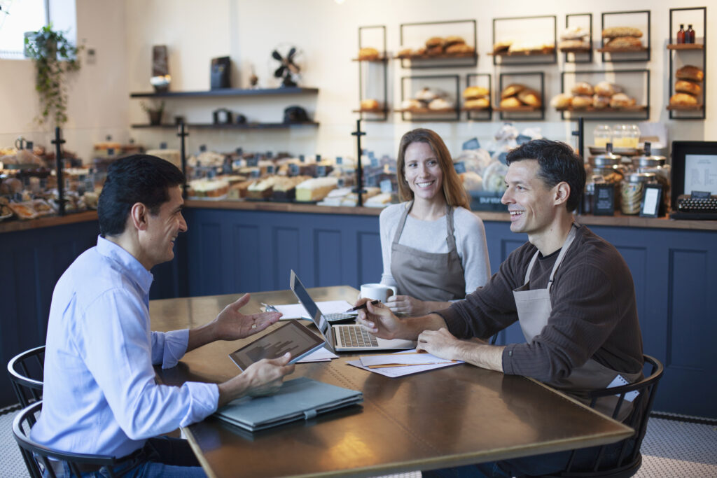 Mature Middle Eastern financial advisor talking with small business owner sitting together in bakery planning their retirement.